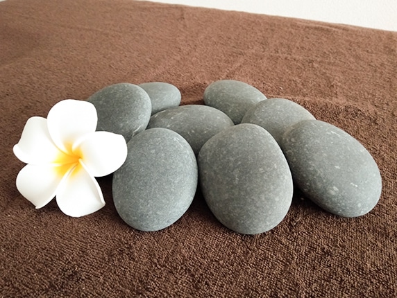 ホットストーンとプルメリアの花が置かれた、落ち着いたサロン空間のイメージ